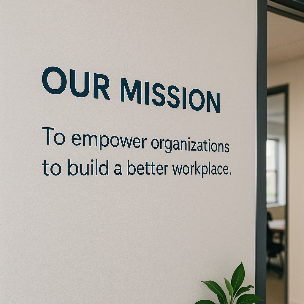 Mission statement painted on a light gray office wall in bold navy text, reading 'Our Mission: To empower organizations to build a better workplace,' with natural light and modern office decor reinforcing a culture-driven workspace.